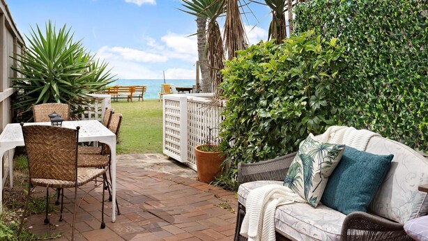 A patio with a wicker table and chairs, a white fence, and a couch with cushions. - Apartment 1 - The Coachhouse (Sydney)