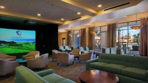 Un hall d’hôtel doté d’un grand écran diffusant des images d’un parcours de golf, de coins salon confortables et de grandes fenêtres offrant une vue sur l’extérieur.