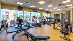 Une salle de sport équipée de divers appareils d’exercice, dotée de grandes fenêtres et d’un écran de télévision.