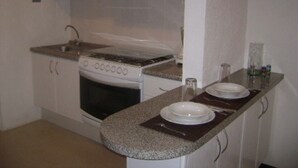 A compact kitchen with white cabinets, a stove, and a countertop with two plates and a glass. - Casa Familiar Acapulco Punta Diamante, Fracc. Puente del Mar, cerca de la playa. (Aeropuerto)