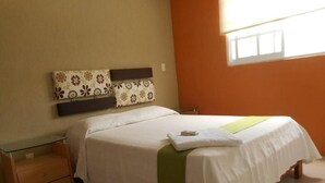A neatly made bed with a white and green bedspread, a wooden nightstand with a drawer, and a wall-mounted shelf with patterned cushions. - Casa Familiar Acapulco Punta Diamante, Fracc. Puente del Mar, cerca de la playa. (Aeropuerto)