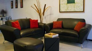 A living room with two black leather sofas, each with a red cushion, and a small black ottoman. There is a framed abstract painting on the wall and a tall plant in the corner. - Casa Familiar Acapulco Punta Diamante, Fracc. Puente del Mar, cerca de la playa. (Aeropuerto)