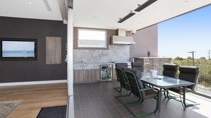 A modern kitchen with a built-in oven, a dining area with a glass table and chairs, and a large window offering a view of the sea. - Bayview Waterfront home Tyrone Foreshore (RYE)