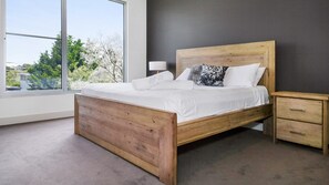 A modern bedroom with a wooden bed, a nightstand, and a view of trees through a large window. - Bayview Waterfront home Tyrone Foreshore (RYE)