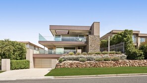 A modern two-story house with a stone facade, a flat roof, and a well-maintained lawn. - Bayview Waterfront home Tyrone Foreshore (RYE)