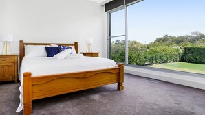 A bedroom with a large bed, wooden headboard, two bedside tables, and a view of a garden through a large window. - Bayview Waterfront home Tyrone Foreshore (RYE)