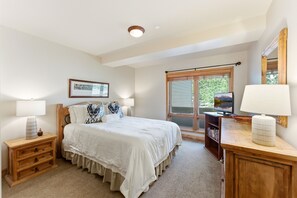 A bedroom with a bed, bedside tables, a dresser, a television, and a window.