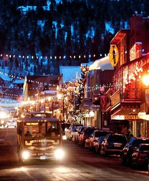 A historic trolley on a city street at night, with buildings and string lights in the background.