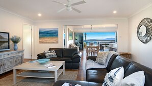 A spacious living room with a view of the sea, a dining area, and a balcony. - Spirit of Gerroa  - Moments from Seven Mile Beach (Gerroa)