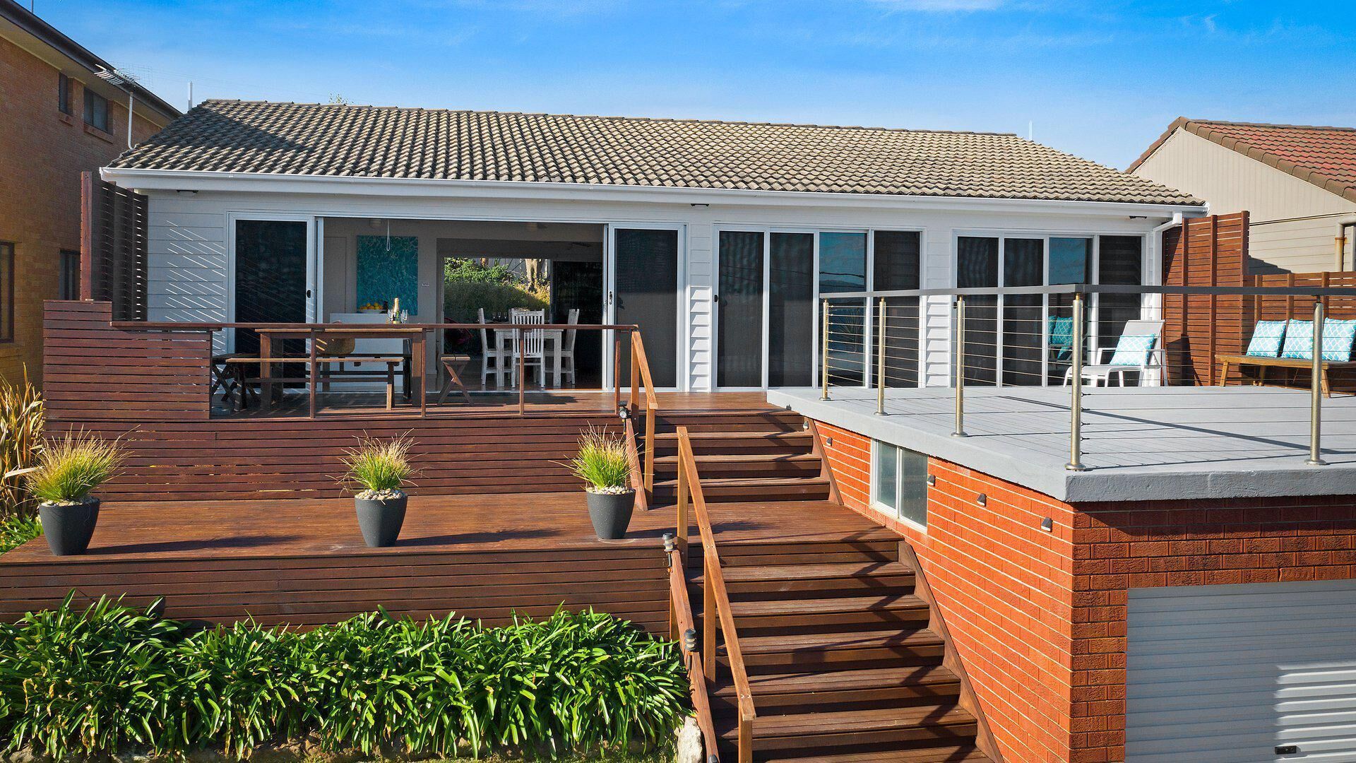 A modern house with a wooden deck, outdoor seating, and a glass-enclosed patio.