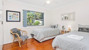 A bedroom with two beds, a large window with a view of greenery, a framed photo collage, and a wicker chair. - Spirit of Gerroa  - Moments from Seven Mile Beach (Gerroa)