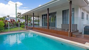 Une maison moderne dotée d’une piscine, de grandes fenêtres et d’un patio couvert.