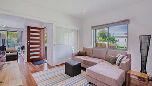 Un salon moderne avec un canapé, un pouf et une grande fenêtre donnant sur l’extérieur.