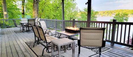 Une terrasse couverte, aménagée avec du mobilier d’extérieur, un foyer et une vue sur un lac.