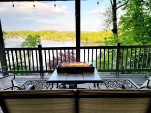 Un espace extérieur am énagé, abrité et doté d’un foyer, offrant une vue sur un lac et des collines boisées.