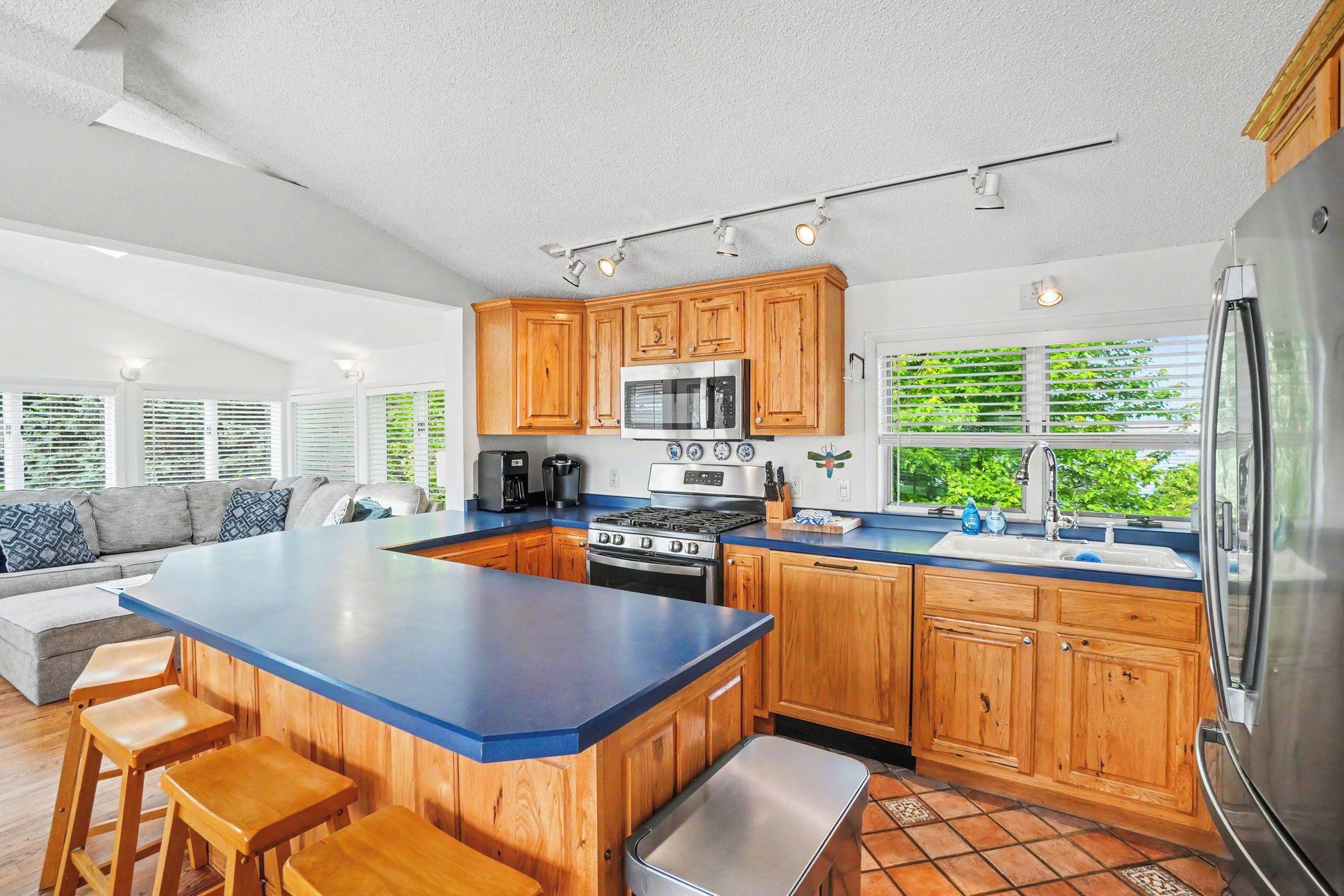 A modern kitchen with wooden cabinets, a large island, and a view of greenery outside.