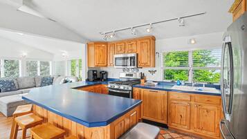 A modern kitchen with wooden cabinets, a large island, and a view of greenery outside.