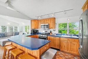 Une cuisine moderne avec des meubles en bois, un grand îlot central et une vue sur la verdure environnante.
