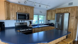 A modern kitchen with wooden cabinets, a large island with bar stools, stainless steel appliances, and a window providing natural light.