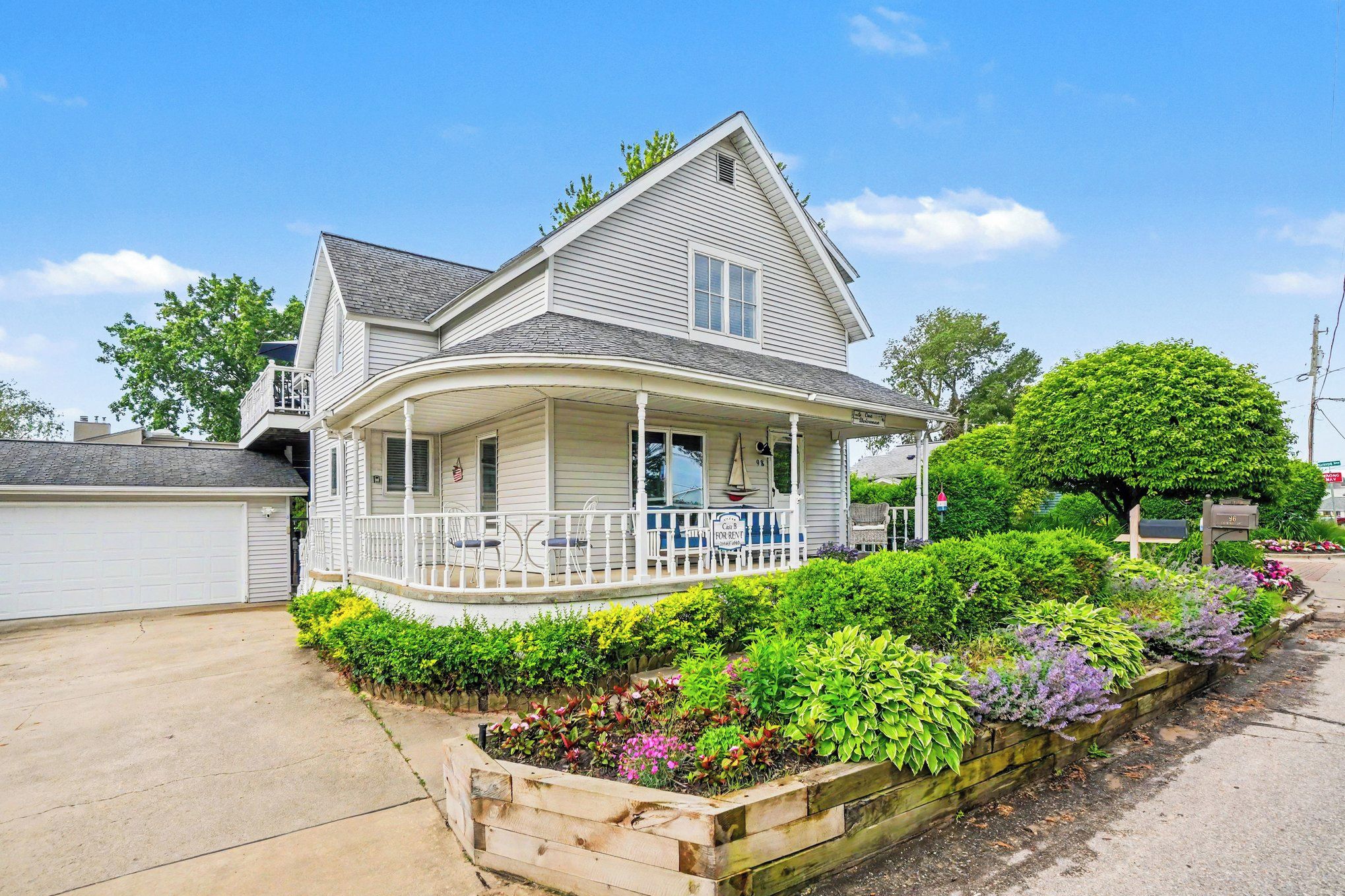 A two-story house with a covered porch, a garage, and a landscaped garden with various plants and flowers.