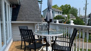 A wooden deck with a round table and four chairs, a white railing, and a gray umbrella.