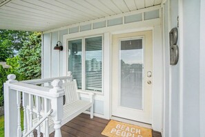 Varanda coberta com um banco, uma porta com olho mágico e um tapete de entrada com a inscrição 'BEACH PEOPLE'.