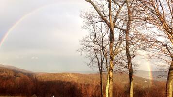 A landscape with a rainbow, trees, and a distant house.