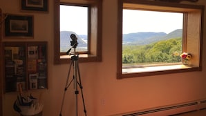 Een kamer met een telescoop op een statief, nabij een raam met uitzicht op een bergachtig landschap.
