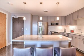 Een moderne keuken met een groot eiland, roestvrijstalen apparatuur en hanglampen.