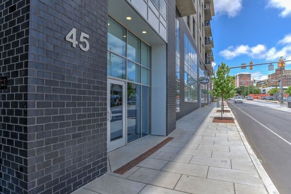 Een modern gebouw met een grote glazen ingang, huisnummer 45, en een trottoir met een boom.