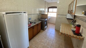 Een keuken met een koelkast, fornuis, gootsteen en een betegelde achterwand.
