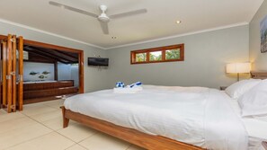 Une chambre d’hôtel avec un lit, un ventilateur de plafond, une télévision, une fenêtre et une porte en bois.