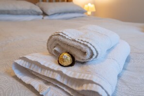 Una toalla blanca doblada con un chocolate envuelto sobre una cama con una colcha estampada.