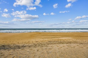 Ein Strand mit weitem Sandbereich und einem klaren Himmel mit vereinzelten Wolken.