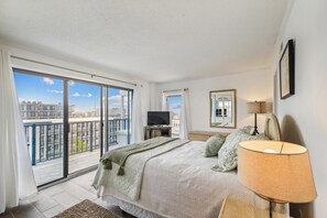 Ein Hotelzimmer mit einem großen Balkon, einem Bett mit weißer Bettdecke, einem Fernseher und einem Spiegel an der Wand.