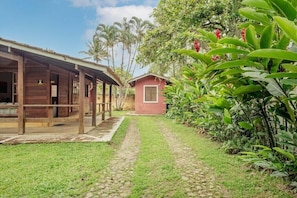 A pathway leading to a wooden building with a red door, surrounded by lush greenery and palm trees.