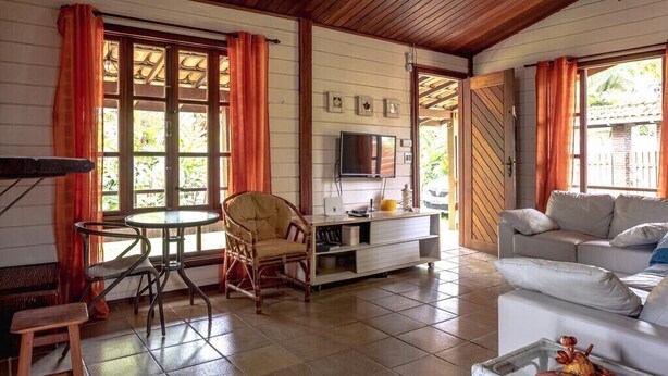 Una sala de estar acogedora con techo de madera, un televisor, un sofá y un comedor con mesa y sillas.