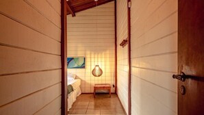 Un estrecho pasillo con paredes de madera y suelo de baldosas que lleva a un dormitorio con una cama y una mesita.