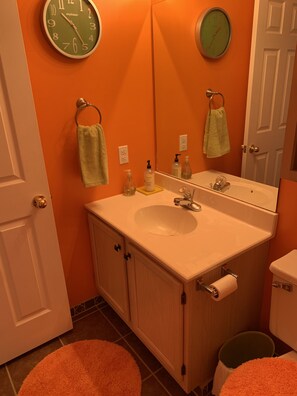 A bathroom with a sink, mirror, and two clocks on the wall. There are towels hanging on hooks and a toilet paper holder. - Modern Style Condo! Amazing view!! (Osage Beach)
