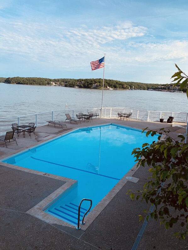 A swimming pool with a flag, surrounded by chairs and tables, overlooking a lake. - Modern Style Condo! Amazing view!! (Osage Beach)