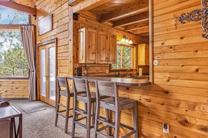 Cozy cabin-style kitchen with a bar area, sink, and appliances, offering a view of the surrounding trees.