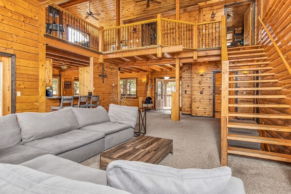 A spacious log cabin interior with a large sofa, a wooden staircase, and a dining area.
