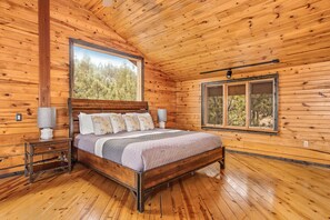 A wooden cabin bedroom with a bed, nightstands, and two windows.
