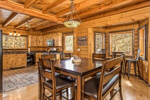 A wooden cabin interior with a dining table, chairs, and a kitchen area.