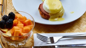 Un plateau de petit-déjeuner avec des œufs Bénédicte, un verre de jus d’orange et un bol de fruits.