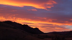 Un coucher de soleil sur un paysage montagneux, avec des collines ondoyantes et un ciel dégagé.