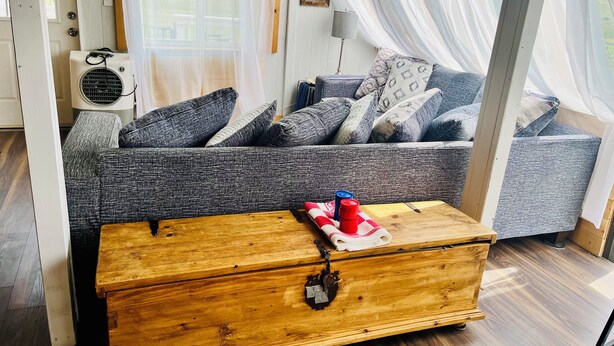 Une pièce chaleureuse avec un canapé gris, une commode en bois et une fenêtre ornée de rideaux légers.