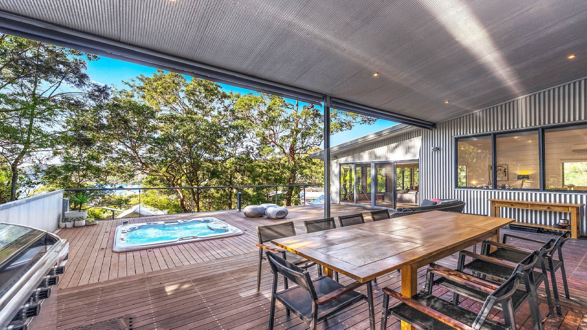 An outdoor deck with a hot tub, wooden table, and chairs, overlooking a forested area.