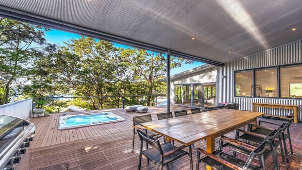 An outdoor deck with a hot tub, wooden table, and chairs, overlooking a forested area.