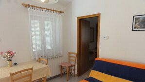 Ein Zimmer mit Esstisch, Stühlen, einer Couch, einem Fenster mit Vorhängen und einer Tür zu einem weiteren Raum.